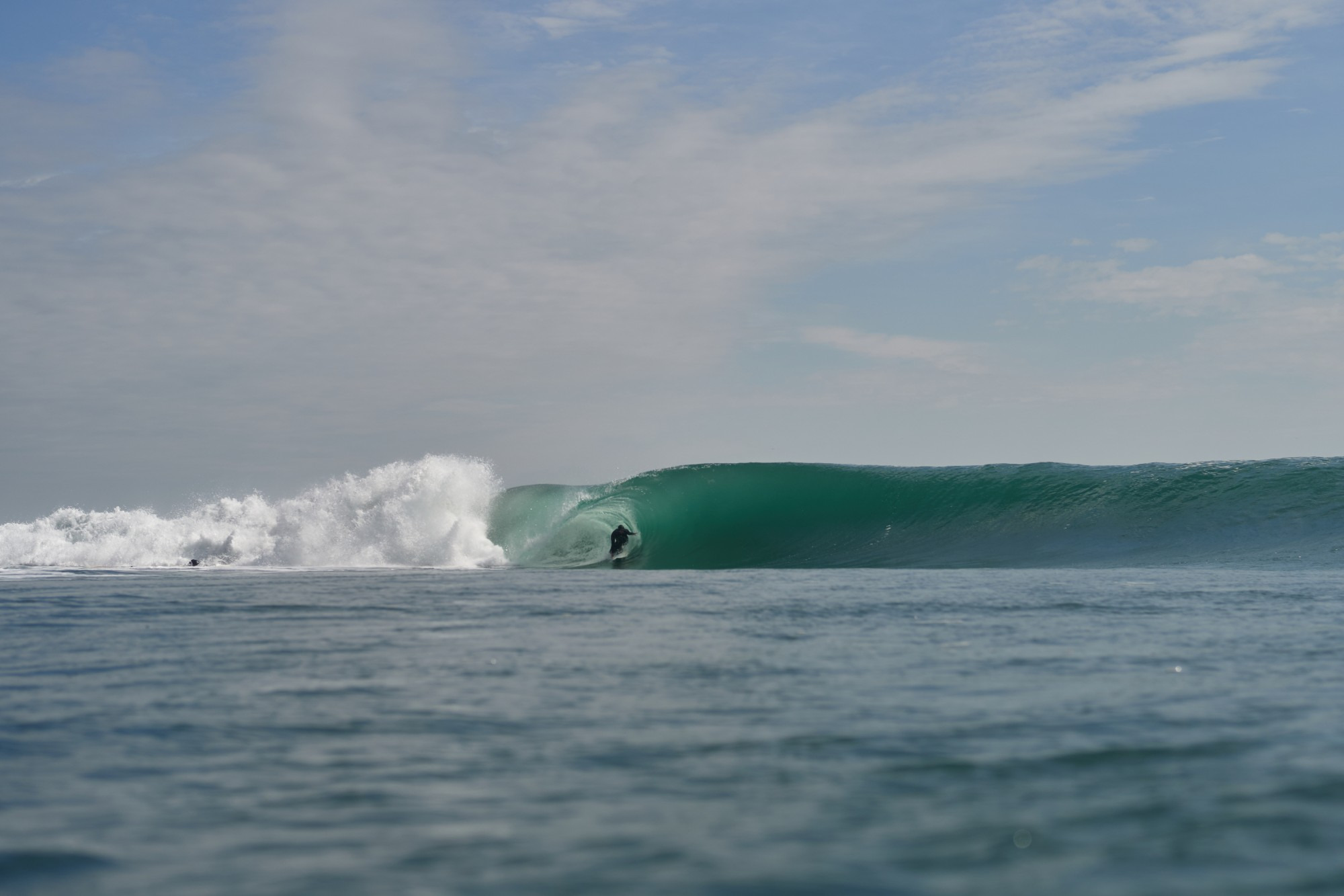 Ola tubular rompiendo en la costa con un surfista dentro